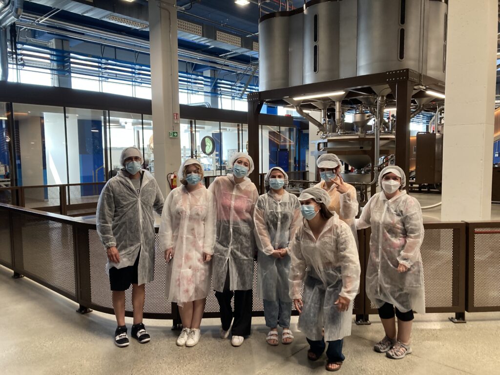 Seven people stand in a factory with hair nets and clothing covers