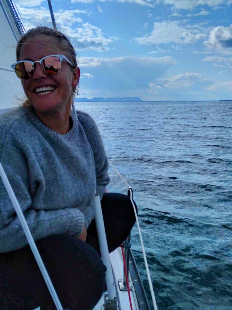 Smiling female on sailboat on Lake Superior with large island in the background